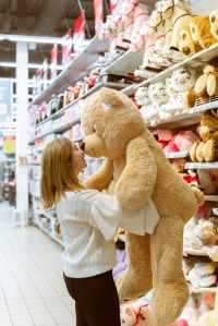 Girl standing holding large teddy bear in front of a shelf of toys